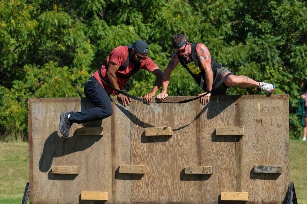 Two athletes tethered together climbing a wooden wall